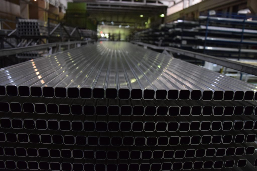 Neatly stacked rows of rounded square, hollow aluminium extrusion profiles in mill finish inside an Australian warehouse.