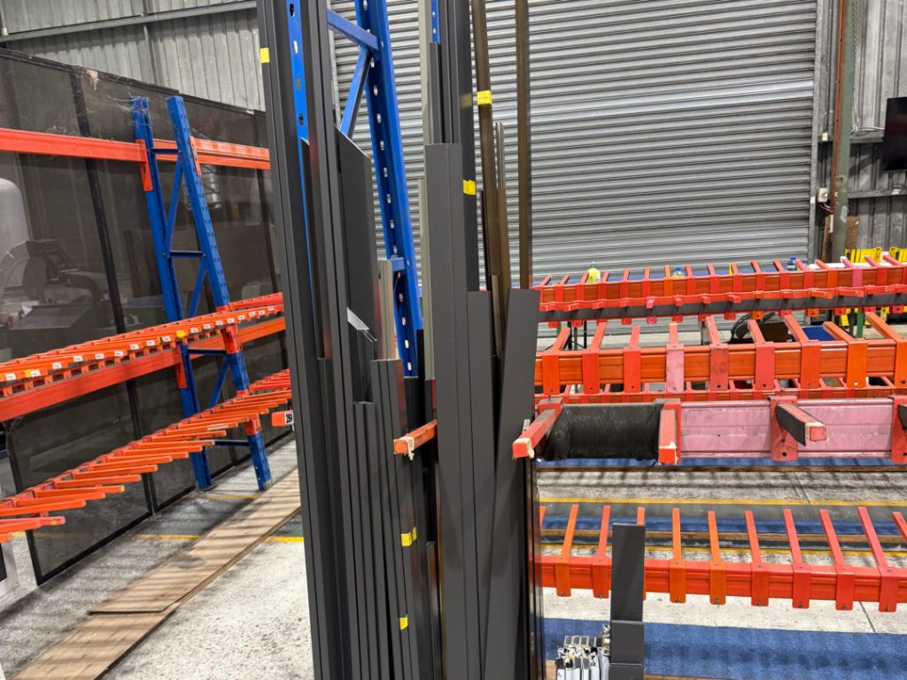 The image shows a close-up view of various aluminium extrusion profiles stacked in a warehouse, highlighting an extensive product range ideal for DIY projects and builders. These profiles, which include flat bars and angles, are designed for strength and flexibility, making them suitable components for a variety of applications across industries in Sydney and Australia.