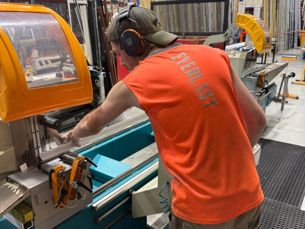 The image shows a man preparing a machine for cutting various aluminium angle and flat bar profiles, showcasing the extensive product range available for DIY projects. These aluminium extrusions are ideal components for builders and fabricators, demonstrating strength and adaptability for diverse applications in industries across Australia.